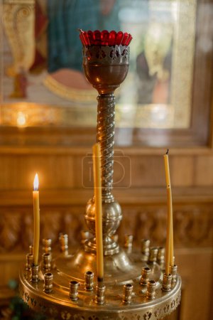 Bronze candlestick with lit candles in an Orthodox church setting. Evokes reverence and solemnity in spiritual ceremonies