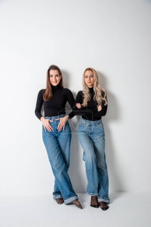 Téléchargez les photos : Deux belles filles brune et blonde posant en studio contre le gris - en image libre de droit