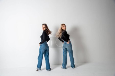 Téléchargez les photos : Deux belles filles brune et blonde posant en studio contre le gris - en image libre de droit