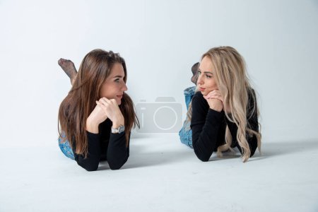 Foto de Dos hermosas chicas morena y rubia posando en estudio contra gris - Imagen libre de derechos
