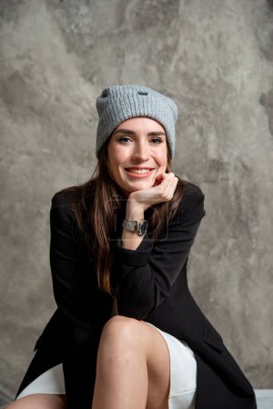 Foto de Hermosa joven posando en estudio con vestido blanco, chaqueta negra y sombrero gris - Imagen libre de derechos