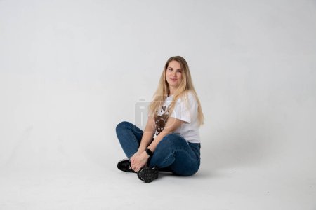 Téléchargez les photos : Beautiful young woman in a white t-shirt and jeans on a gray background - en image libre de droit