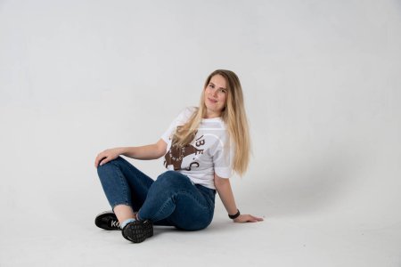 Téléchargez les photos : Beautiful young woman in a white t-shirt and jeans on a gray background - en image libre de droit