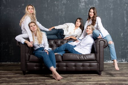 Téléchargez les photos : Group portrait of five attractive Caucasian women wearing white shirts and jeans posing on sofa. - en image libre de droit