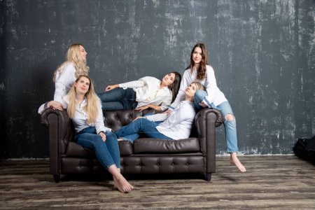Photo for Group portrait of five attractive Caucasian women wearing white shirts and jeans posing on sofa. - Royalty Free Image