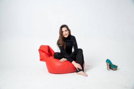 Photo for Beautiful young woman in black clothes posing on bean bag chair on a white background - Royalty Free Image