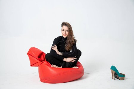 Photo for Beautiful young woman in black clothes posing on bean bag chair on a white background - Royalty Free Image