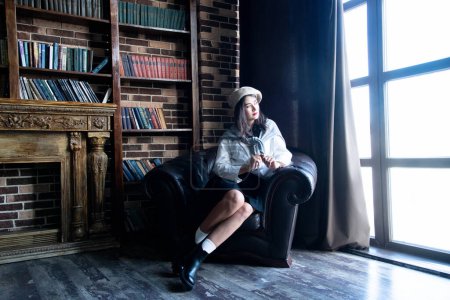 Photo for Portrait of a woman wearing beret sitting on a chair with books - Royalty Free Image