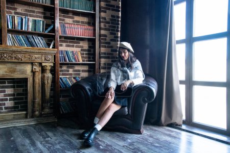 Téléchargez les photos : Portrait of a woman wearing beret sitting on a chair with books - en image libre de droit