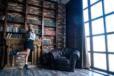 Téléchargez les photos : Young attractive girl standing near the bookshelf - en image libre de droit