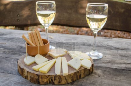 Foto de Muestrario de queso de cabra y vino blanco servido en una tabla de madera. - Imagen libre de derechos