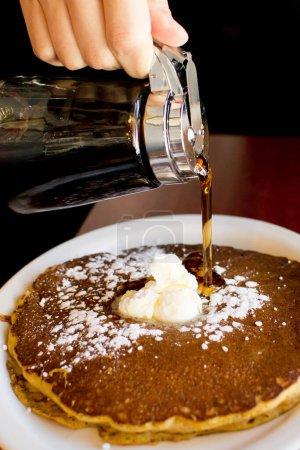 Photo for Pouring maple syrup on a stack of pancakes with butter and powdered sugar. - Royalty Free Image
