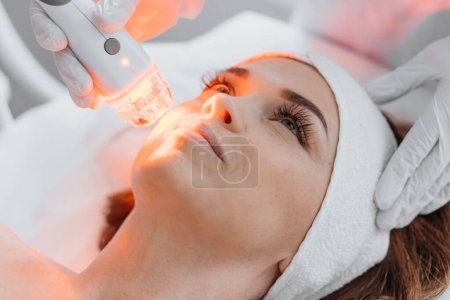Photo for Photo from the studio of cosmetology, demonstrating the process of led therapy and facial skin care. A woman undergoes a procedure in a beauty salon. Beautician in white gloves use. High quality photo - Royalty Free Image