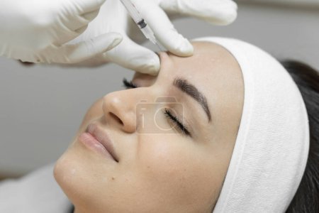 Photo for Injection with a syringe with butolin on a womans face. Care with love: a woman visits a beautician for botulinum therapy, which makes her skin soft, smooth and youthful. Beauty clinic. High quality - Royalty Free Image