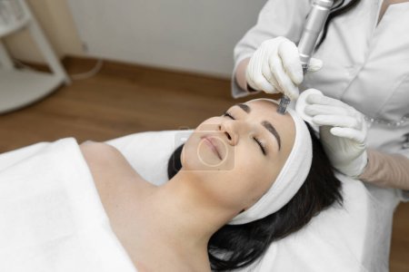 A professional cosmetologist uses innovative fractional mesotherapy to improve the condition of the skin in a beauty salon. The young woman is relaxed and rests during cosmetic procedures. High