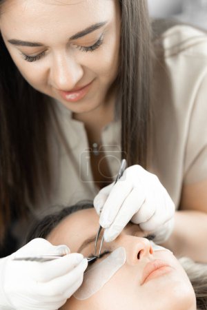 The photo shows the moment when the beautician completes the eyelash extensions by adding the finishing touches to the gorgeous look. The result is naturally attractive eyelashes that emphasize the