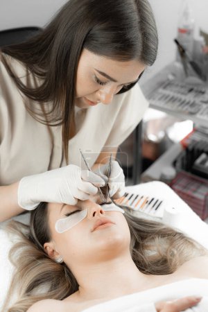 The photo shows a beautician who with great attention and professionalism extends eyelashes, giving his client a charming and luxurious look. Woman in beauty salon on eyelash extension procedure. High
