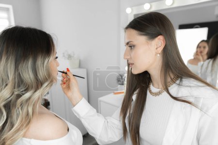 Photo for The photo conveys an exclusive moment when a young woman trusts her face to a makeup artist. The professional skills of a makeup artist turn her into an unsurpassed beauty, emphasizing her uniqueness - Royalty Free Image