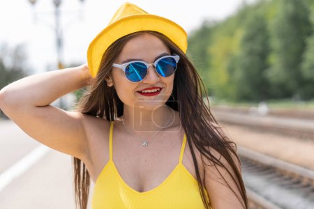 Téléchargez les photos : L'image d'un voyageur : une femme en tenue jaune joyeuse avec des lunettes se prépare à des impressions incroyables et des surprises lors de son voyage. En attente de transport : une femme en jaune avec des lunettes - en image libre de droit