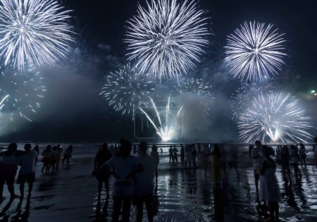 Foto de Fireworks on the beach. People watching watching the explosion of fireworks during the celebration of the new year. Santos City, Brazil. - Imagen libre de derechos