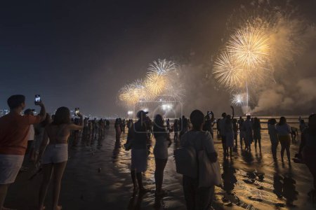 Foto de Fireworks on the beach. People taking pictures with cell phones and watching fireworks during the New Year celebration. Santos city, Brazil. 01 de janeiro de 2023. - Imagen libre de derechos