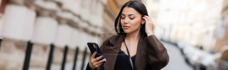 Téléchargez les photos : Jeune femme brune regardant mobile sur la rue floue dans la prague, bannière - en image libre de droit