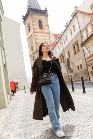 brunetka kobieta w brązowym płaszczu i dżinsy spacery wzdłuż starożytnej ulicy w Pradze