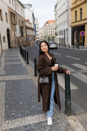 Volle Länge des stilvollen Reisenden hält Pappbecher in der Nähe der Straße in Prag