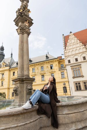 Junge Frau mit Pappbecher in der Nähe der Statue des heiligen Josef und des Brunnens auf dem Karlsmarkt in Prag 