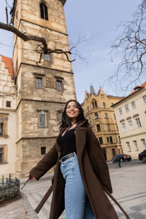 Téléchargez les photos : Voyageur brunette positive tenant des lunettes de soleil dans la rue à Prague - en image libre de droit