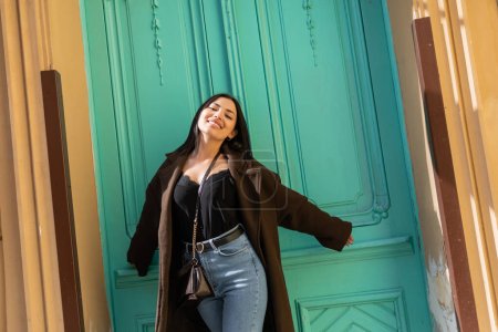 Cheerful traveler looking at camera near turquoise door of building on street in Prague 