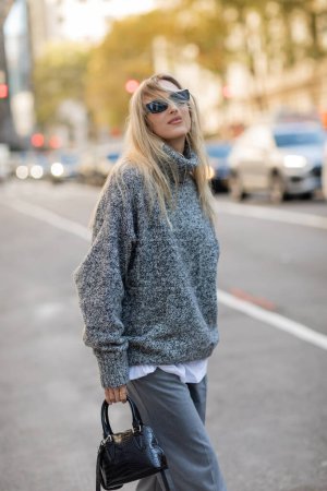 Téléchargez les photos : Femme heureuse dans des lunettes de soleil et tenue à la mode tenant sac à main tout en se tenant debout sur la rue de New York - en image libre de droit