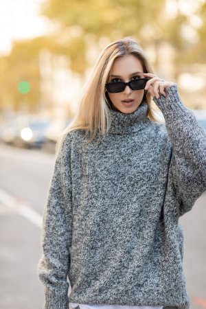 Porträt einer blonden Frau im grauen Pullover mit trendiger Sonnenbrille auf der Straße von New York 