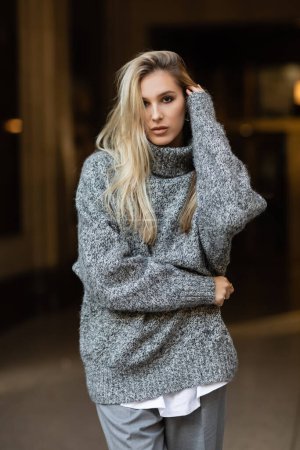 Téléchargez les photos : Jeune femme blonde en tenue grise regardant la caméra tout en posant dans la rue de New York en hiver - en image libre de droit