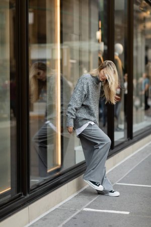 Junge Frau in schickem grauen Outfit steht in New York in voller Länge vor einem Schaufenster 