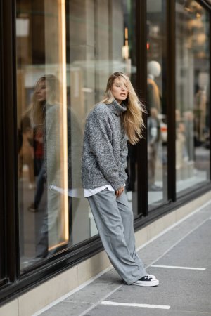 junge Frau in stylischem Winteroutfit, die in der Nähe von Schaufenstern in New York steht 