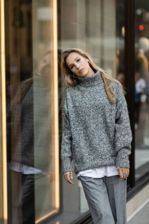 mujer joven en traje gris apoyada en la pantalla de la ventana en Nueva York 