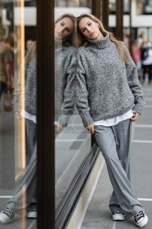 Junge Frau im grauen Outfit lehnt an Glasvitrine in New York 