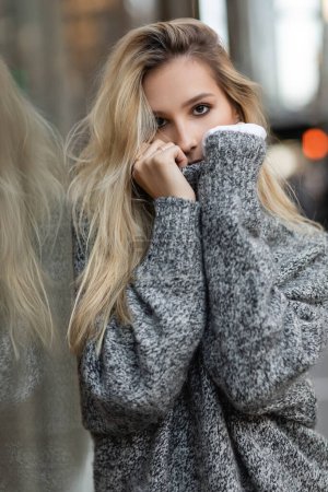 blonde young woman in winter sweater posing near window display in New York 