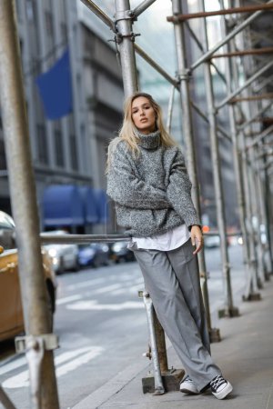 Junge Frau in grauem Winteroutfit lehnt in New York an Straßenlaterne und Autos 