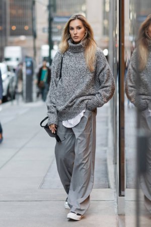 Téléchargez les photos : Pleine longueur de femme blonde en pull d'hiver portant des lunettes de soleil et un sac à main dans la rue urbaine de New York - en image libre de droit