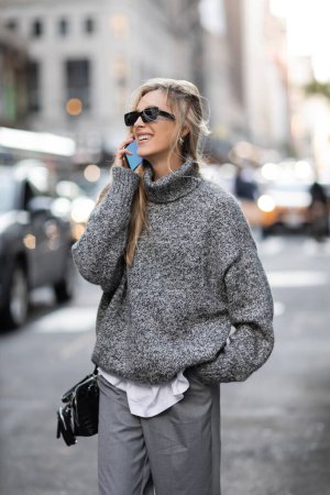 Téléchargez les photos : Femme heureuse en pull d'hiver et lunettes de soleil parler sur smartphone à New York - en image libre de droit