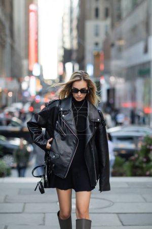Blonde Frau in Lederjacke und trendiger Sonnenbrille auf der Straße von New York 