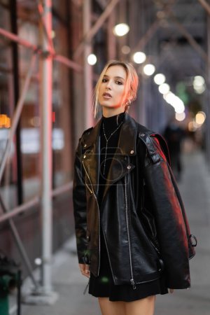 mujer rubia en chaqueta de cuero negro de pie en la calle en la ciudad de Nueva York a la hora de la noche