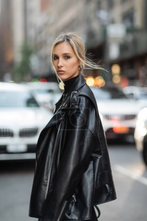 Photo for Portrait of blonde woman in stylish leather jacket looking at camera on urban street in New York - Royalty Free Image