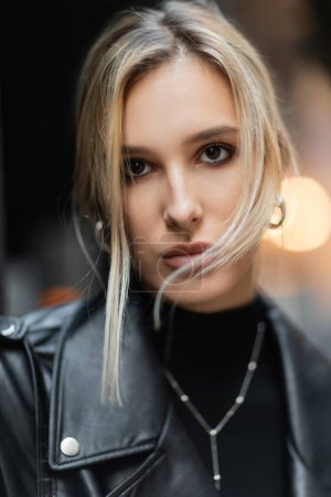 portrait of pretty blonde woman in black leather jacket looking at camera outside 