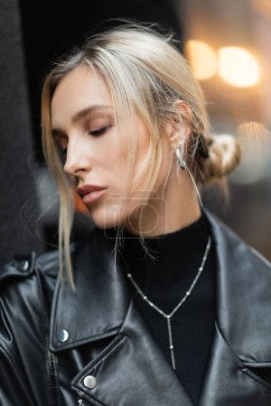 portrait of blonde woman in black leather jacket standing with closed eyes outside 