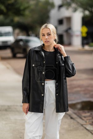 young blonde woman in stylish outfit looking at camera while standing on street in Miami 