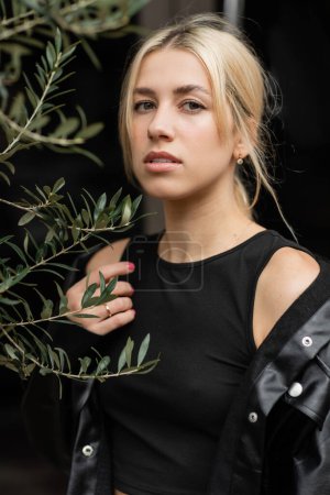 Téléchargez les photos : Portrait de femme blonde veste chemise en cuir debout près de la plante - en image libre de droit