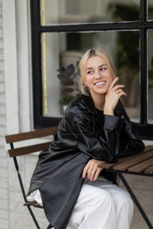 Téléchargez les photos : Joyeuse jeune femme en veste chemise en cuir assis dans un café extérieur dans la rue à Miami - en image libre de droit